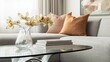 © Saowanee - High angle shot of a modern glass coffee table decorated with books and a vase of flowers, placed in front of a gray sofa. The background and soft lighting create a warm and modern atmosphere.
