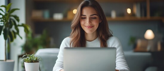 Wall Mural - A young woman smiles while working on her laptop at home.