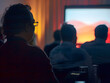 © Moon Story - person is attentively watching presentation displayed on projector screen, surrounded by audience in dimly lit room. atmosphere conveys focus and engagement