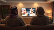 © Tark - back view of a Saudi family watching tv in the living room and sitting on a couch, back view. Generative AI