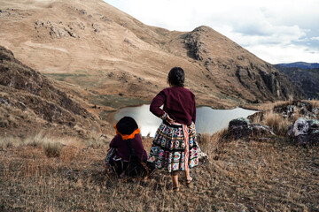 Two Quechua women in traditional clothing looking at a lake in the Andes Mountains, Sacred Valley, Peru