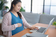 © Charlie's - Pregnant asian woman using laptop at home pregnant businesswoman typing on laptop working on remote project in home office pregnancy