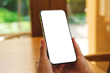 Wall Mural - Mockup image of a woman holding and using mobile phone with blank desktop at home