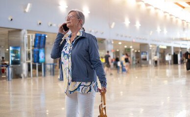 Senior woman travels at airport looking attime table towards board gate. Portrait of elderly happy traveler enjoying trip and vacation