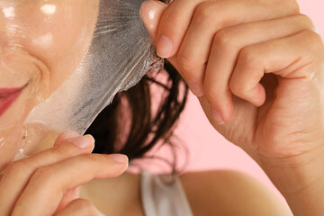 Canvas Print - Woman peeling off face mask on pink background, closeup