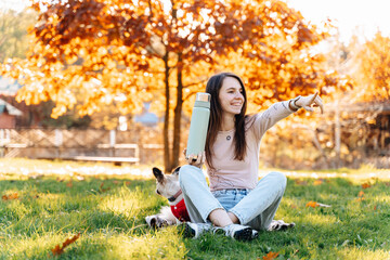 Young woman pouring tea from thermos into cup in autumn park