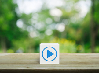 Wall Mural - Play button icon on white block cube on wooden table over blur green tree in park, Business music online concept