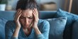 © Oulailux - A person sitting on a couch, holding their head in discomfort, with subtle expression of nausea. Dim lighting and blurred surroundings emphasize the overwhelming feeling of headache and sickness.
