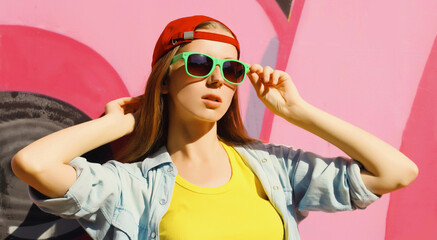 Wall Mural - Stylish young girl in baseball cap, glasses, modern teenager girl posing against the graffiti wall