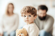 © Victoria - Sad young boy is holding his teddy bear while his parents are arguing in the background