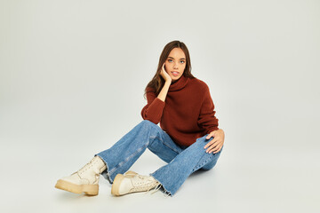 Young woman sits on the floor, dressed in a stylish sweater and jeans, radiating warmth.