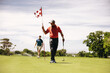 © Jacob Lund - Golfers walking on putting green, holding golf clubs and flagstick