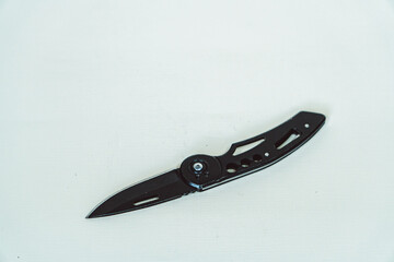 Mini size folding knife of solid black color partially opened isolated on white background. Close-up view of a black folding knife used for various outdoor or survival activities