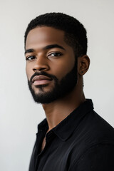 
Headshot of a Black mixed race male model with short hair and a beard, wearing a dark shirt on a light background