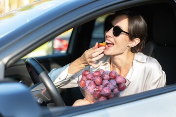 Woman enjoying plums in a car on a sunny day.