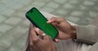 © m-art - A man uses a mobile phone with a green screen sitting outdoors, close-up of his hands, an unrecognizable person
