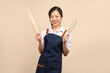 © PBXStudio - Beautiful Asian woman in apron holding kitchen utensils isolated on beige background