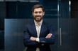 © Tetiana - Portrait of a sleepy young businessman standing in the office, arms crossed on his chest, confidently and smilingly looking at the camera