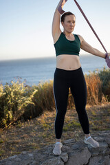 Wall Mural - Athletic woman exercising with resistance band outdoors by the sea