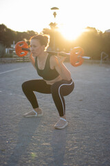 Wall Mural - Woman lifting weights doing squats exercising outdoor at sunset