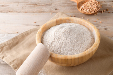 Buckwheat flour in a wooden bowl and raw buckwheat grain on cotton napkin on rustic wooden table background. Alternative flour, gluten free flour, healthy nutrition