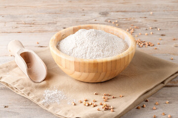 Buckwheat flour in a wooden bowl and raw buckwheat grain on cotton napkin on rustic wooden table background. Alternative flour, gluten free flour, healthy nutrition