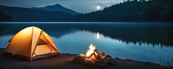 Wall Mural - tent by the lake at night with a warm campfire glow.