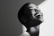 © Anastasia - A black woman joyfully smiles, bathed in soft light, showcasing minimalism and the beauty of her features in a monochromatic setting