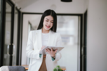 A happy Asian female businessman is at a modern desk. Financial reports and online documents using laptops She analyzed the organization's strategy and cooperated with her team for success.