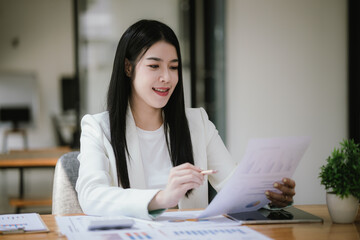 A happy Asian female businessman is at a modern desk. Financial reports and online documents using laptops She analyzed the organization's strategy and cooperated with her team for success.