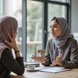 © Alex Pios - Serious young Arab manager woman in hijab talking to female business colleague in office meeting room space with large table, explaining teamwork, project management, speaking, moving hand