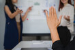 © Kritdanai - A Hand Raised:  A woman's hand reaches towards the board, capturing a moment of proactive engagement and active participation in a modern business meeting. This image evokes a sense of curiosity.