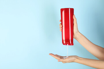 Wall Mural - Woman pouring shampoo onto hand on light blue background, closeup. Space for text