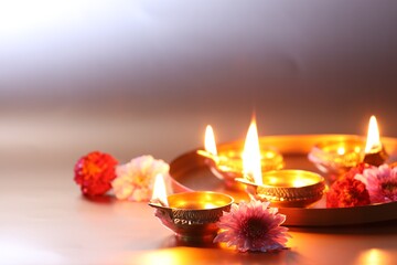 Wall Mural - Diwali celebration. Diya lamps and beautiful flowers on light background, closeup. Space for text