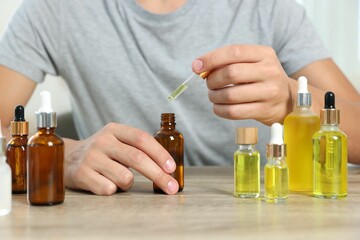 Canvas Print - Young man dripping CBD tincture into bottle from dropper at wooden table, closeup