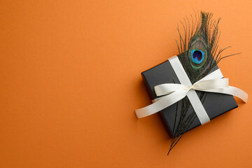 Poster - Beautiful gift box and peacock feather on orange background, top view. Space for text