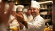 © Олег Фадеев - A joyful male chef in a professional kitchen setting, wearing a traditional white chef's hat and jacket, is clapping