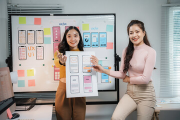 Two asian uiux designers are discussing the development of a mobile app wireframe in their office