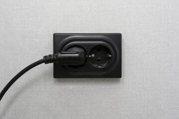 A black charger is currently plugged into a wall socket for power