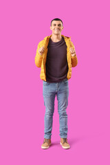 Wall Mural - Young man in warm puffer jacket on purple background