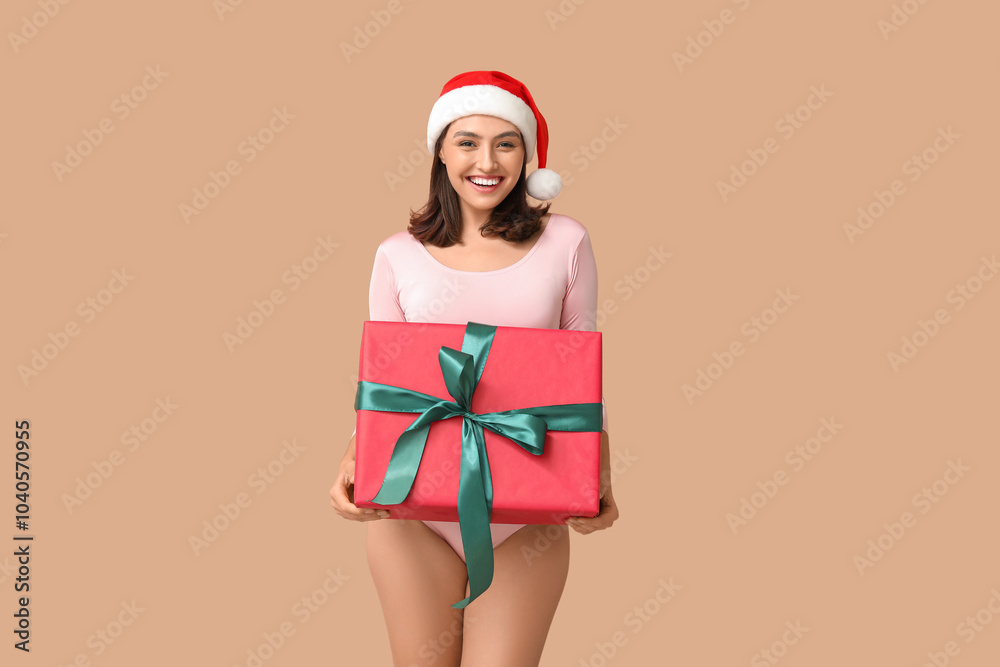 Female gymnast in Santa hat with gift box on brown background
