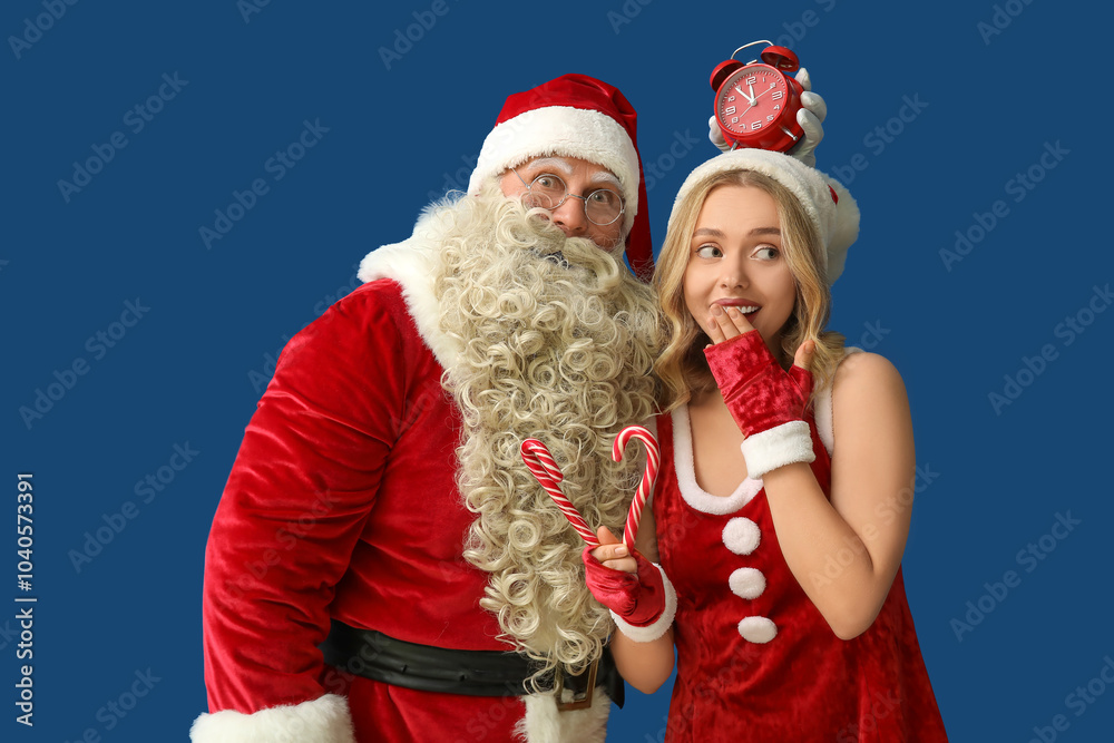 People dressed as Santa Claus with alarm clock and candy canes on blue background