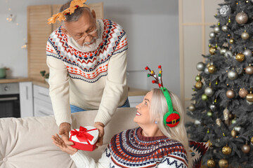 Canvas Print - Mature man greeting his wife with Christmas gift at home