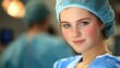 © Anna - A young healthcare worker in surgical scrubs and a cap looks confidently at the camera while supporting a team in a busy hospital environment, ready for an important procedure