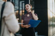 © qunica.com - A confident businesswoman holding a blue folder engages in a discussion during an outdoor meeting, symbolizing professionalism and communication.
