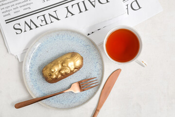 Canvas Print - Plate with sweet eclair, tea and newspaper on light  background