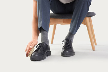 Poster - Businessman with brush cleaning shoes on light background, closeup