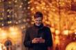 © Zamrznuti tonovi - Jolly young man texting messages on street on new year's eve.
