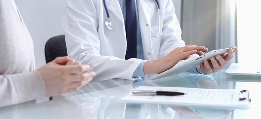 Doctor consultation with patient in modern clinic. Healthcare professional discusses medical information with a woman, holding a tablet computer. Medicine