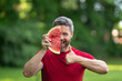 © Volodymyr - Male face with watermelon, close up. Funny man eating watermelon outdoors in summer park. Man eating watermelon. 40s man eat fruit outdoors. Man enjoying watermelon.